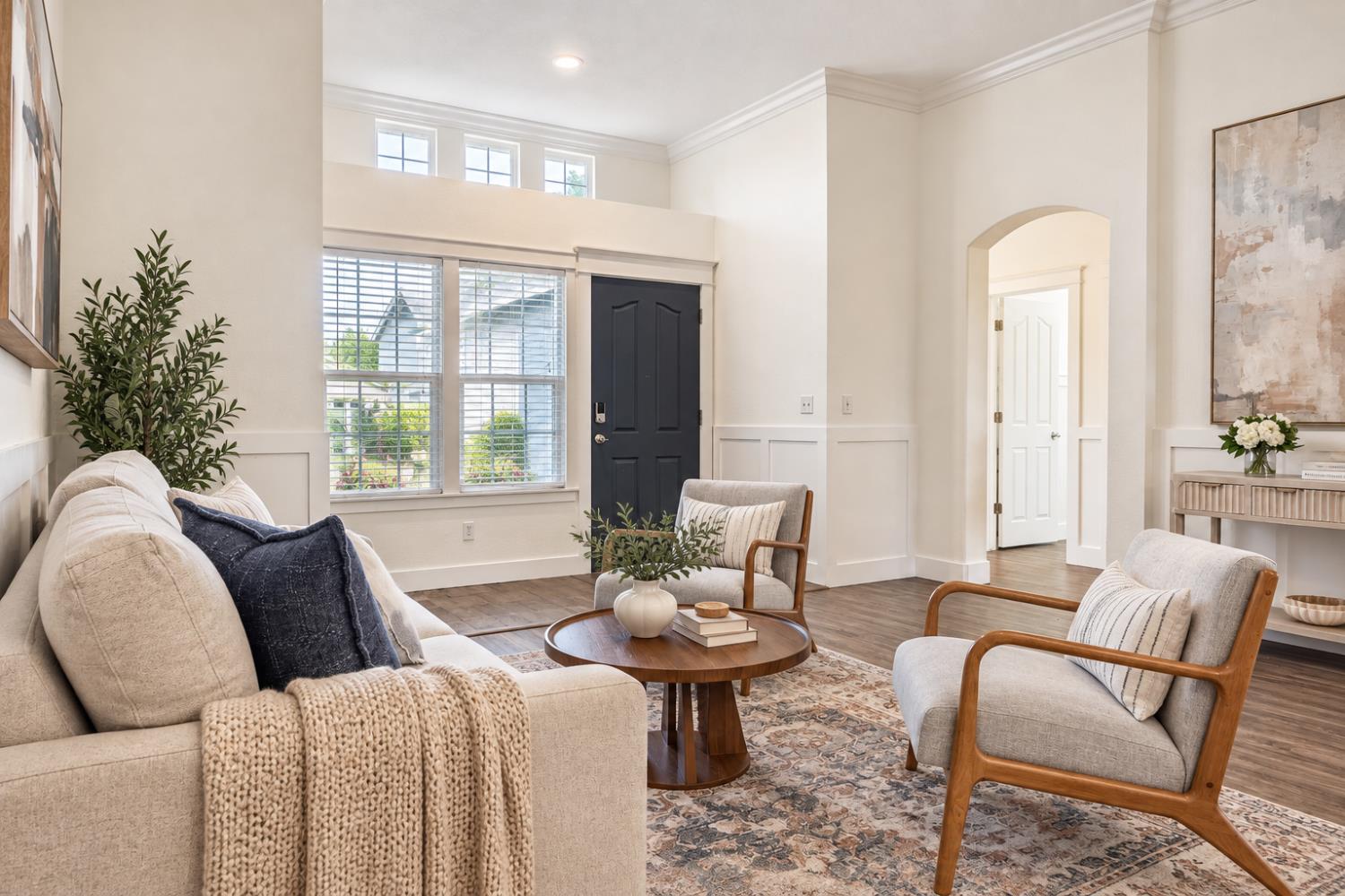 Neutral living room with a cream sofa, wood-framed chairs, and a dark front door